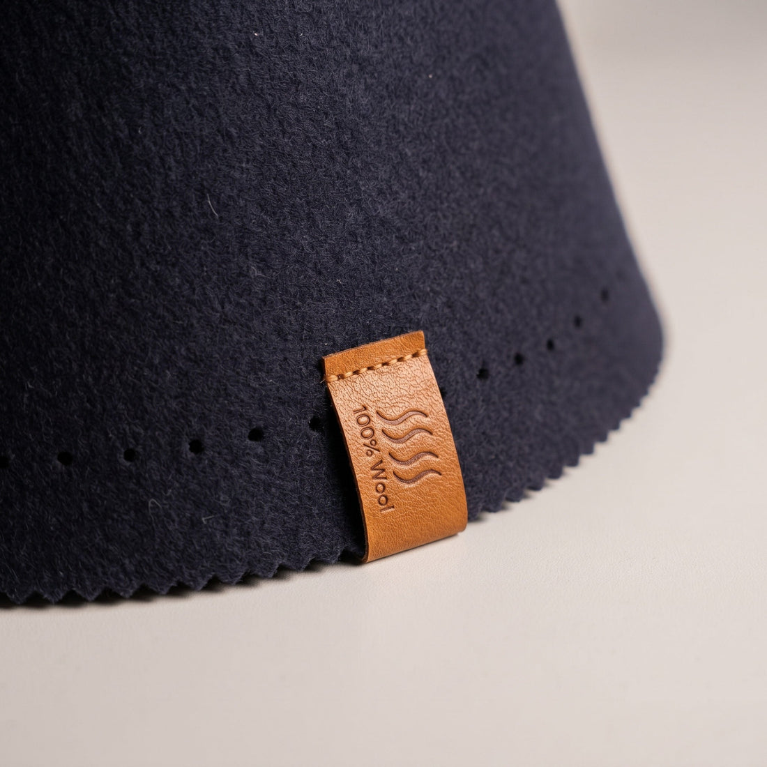 Close-up of the tan 100% Wool leather tag stitched to the brim of a navy sauna hat